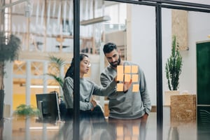 Female and male coworkers pointing at sticky notes on glass window wall